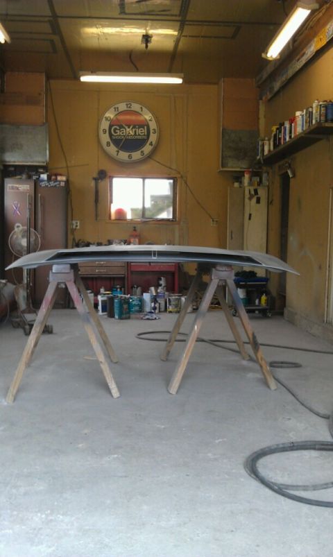 Car hood on sawhorses in a garage with a Gabriel clock on the wall