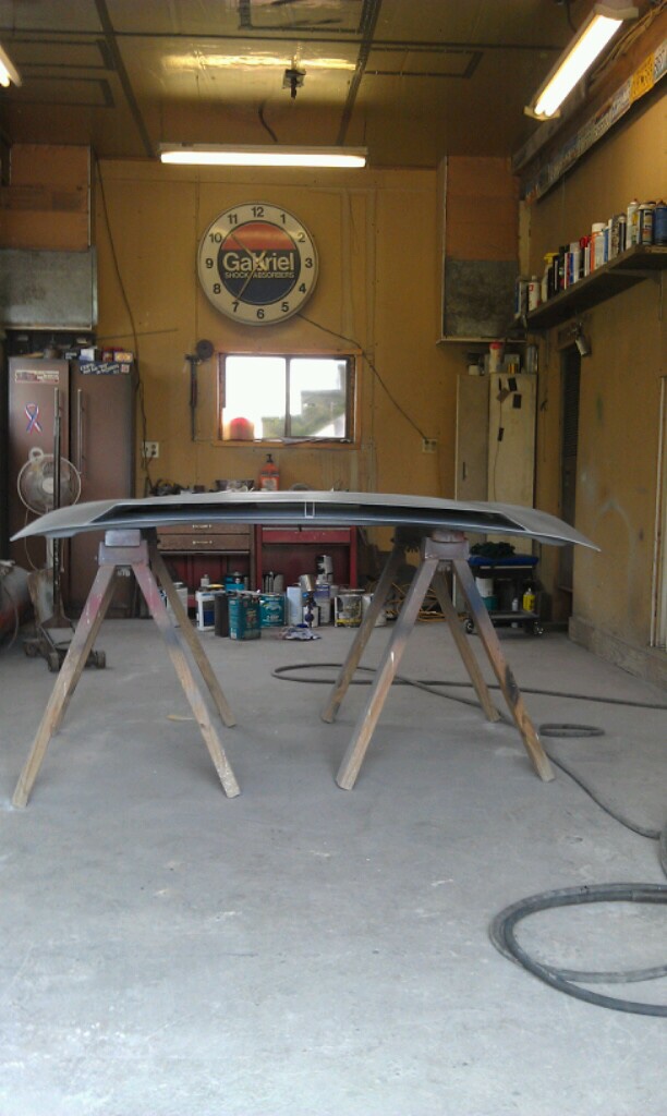 Car hood on sawhorses in a garage with a Gabriel clock on the wall