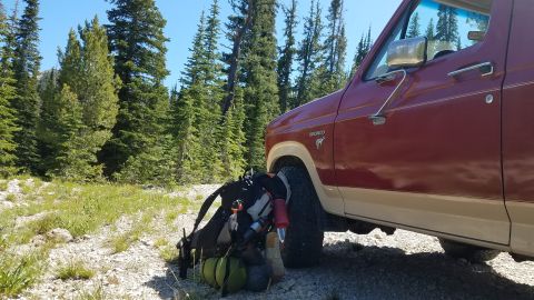 1985 Ford Bronco - A Ford Bronco sits parked on a gravel road in a wooded area, ready for a backpacking trip.