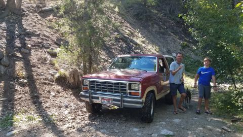 1985 Ford Bronco - 1985 Ford Bronco parked on a dirt road in a wooded area with two people standing nearby.