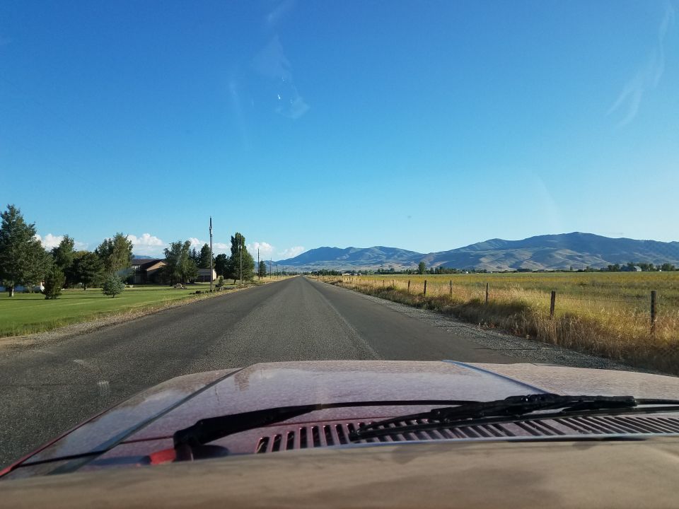 Red vehicle dashboard and windshield view of a long, straight road through a rural landscape