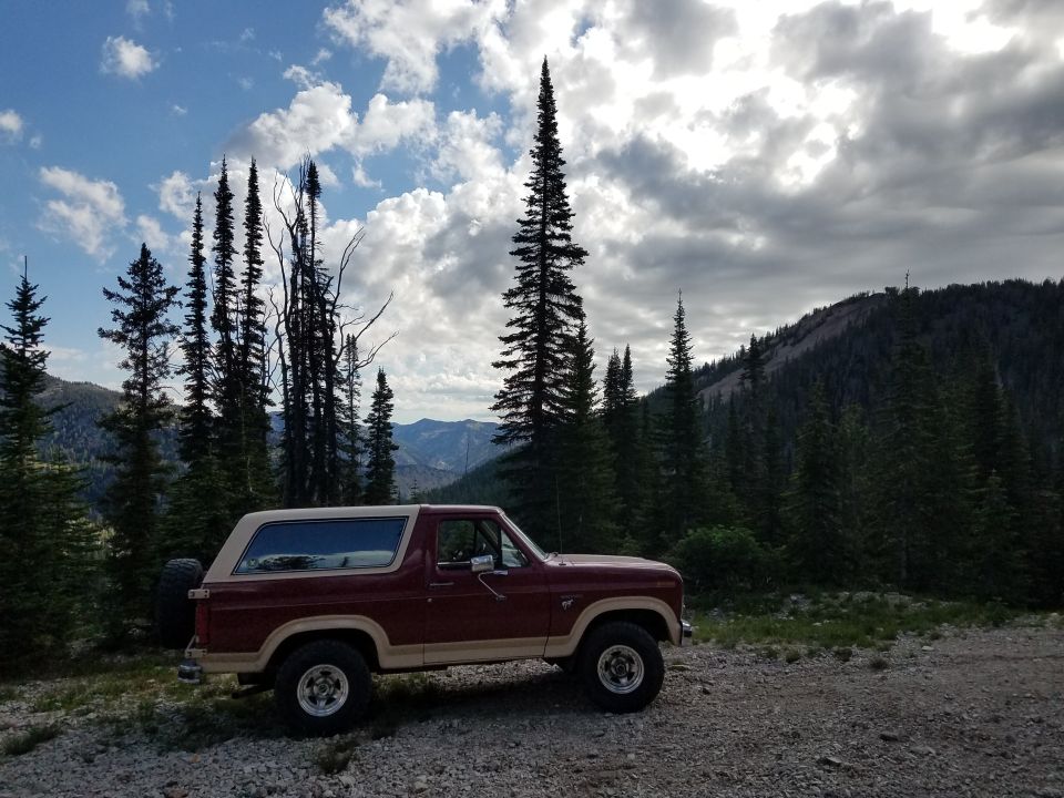 1985 Ford Bronco side view, red and tan, parked in mountain landscape