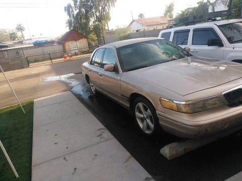 1997 Mercury Grand Marquis - A gold 1997 Mercury Grand Marquis is seen from the front-three-quarter angle, with another vehicle partially visible in the background.