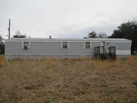 2008 Ford Focus - A long, gray mobile home sits on a foundation with dry grass in the foreground under an overcast sky.