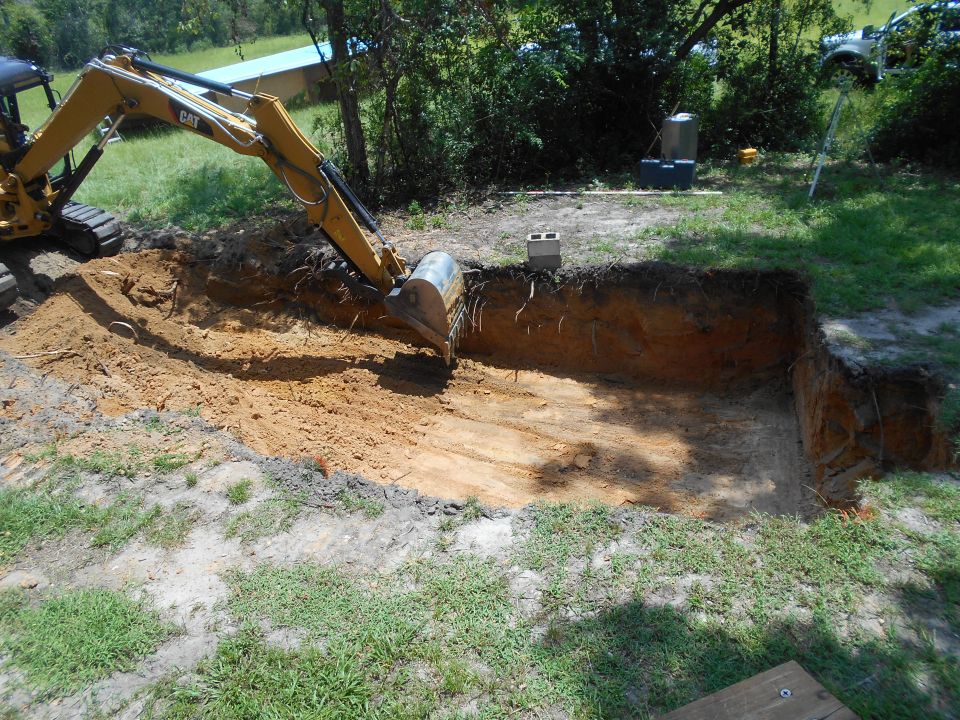 Excavator digging a large hole in a grassy area