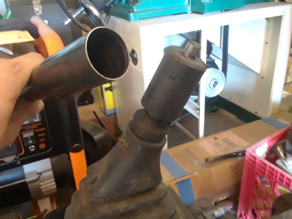 Hand holding metal pipe over black rubber gear shifter boot and metal shaft