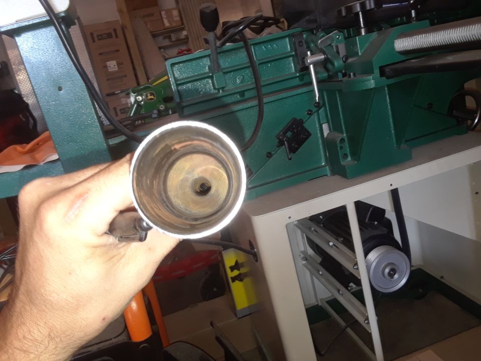 Hand holding a dirty metal pipe in front of a green machine with a motor