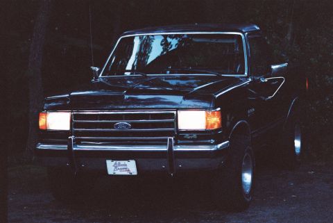 1988 Ford Bronco - Front view of a black 1988 Ford Bronco with headlights on, parked outdoors.