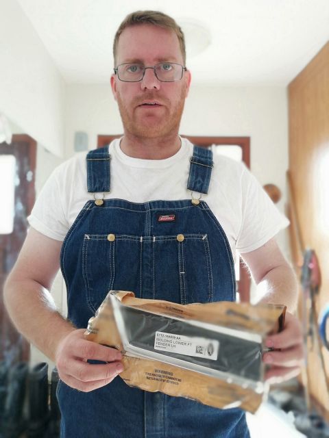 1996 Ford Bronco - A man presents a car part, identified as a lower front fender molding for the left side.