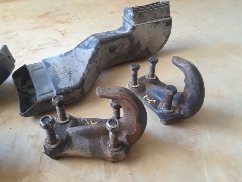 1994 Ford Bronco - Two rusty tow hooks and a black plastic air intake duct are laid out on a concrete surface.