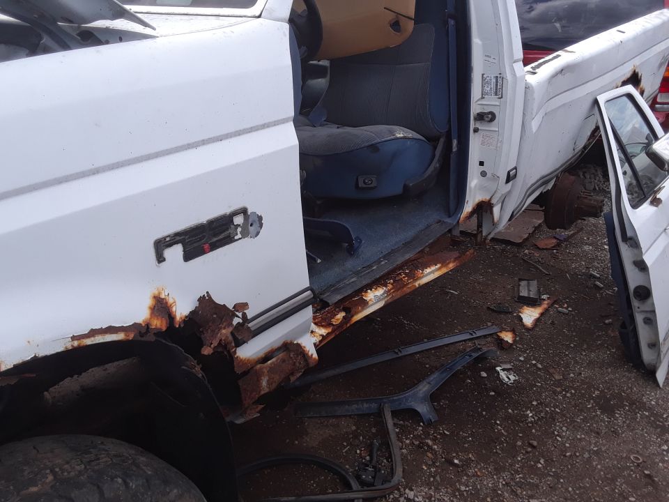 White pickup truck with extensive rust on the lower body and door, showing the interior driver's seat and door panel