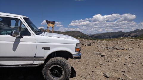 1995 Ford Bronco - A white 1995 Ford Bronco is parked on a rocky mountain summit under a blue sky with scattered clouds.