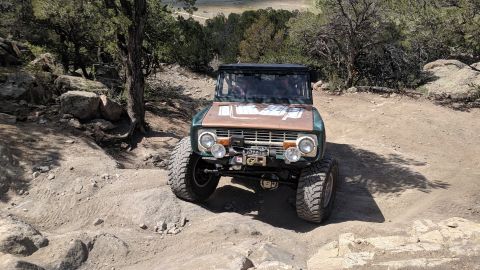 1995 Ford Bronco - First-gen Ford Bronco tackling a challenging off-road course with large tires and modifications.