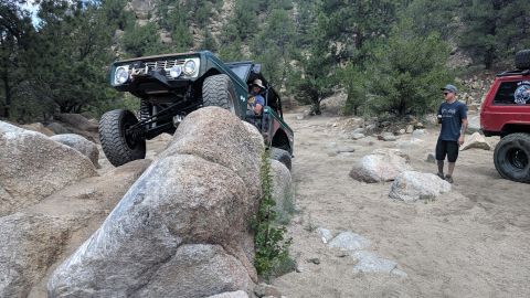 1995 Ford Bronco - A modified green Ford Bronco tackles a challenging rocky trail, with other off-road vehicles present.