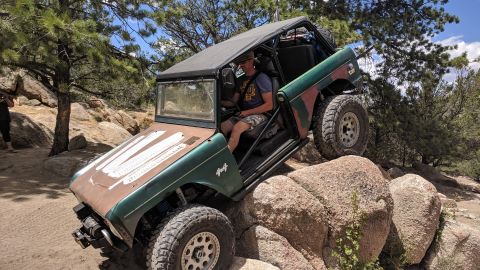 1995 Ford Bronco - This heavily modified off-road vehicle navigates a rocky trail with a driver inside.