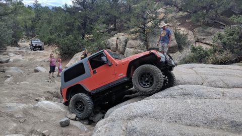 1995 Ford Bronco - An orange Jeep Wrangler TJ tackles a challenging rocky trail, with another vehicle visible in the background.