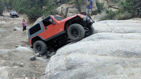 1995 Ford Bronco - Jeep Wrangler tackling a difficult off-road course with spectators watching.