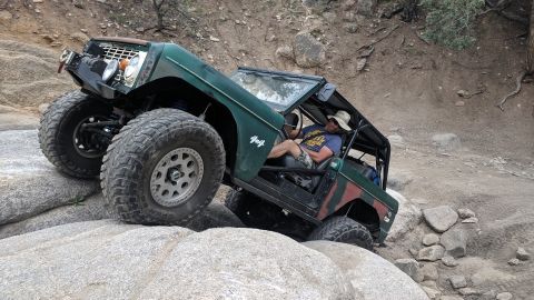 1995 Ford Bronco - Modified off-road vehicle navigates rocky terrain with a driver at the wheel.