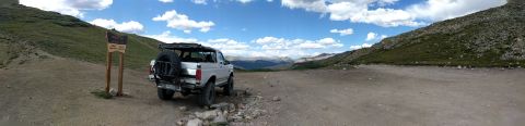 1995 Ford Bronco - A white SUV is parked on a dirt road in a mountainous landscape under a cloudy sky.