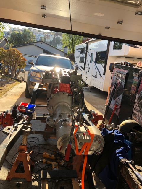 1992 Jeep Wrangler - Engine and transmission assembly undergoing work in a driveway, with a gray SUV and RV visible in the background.
