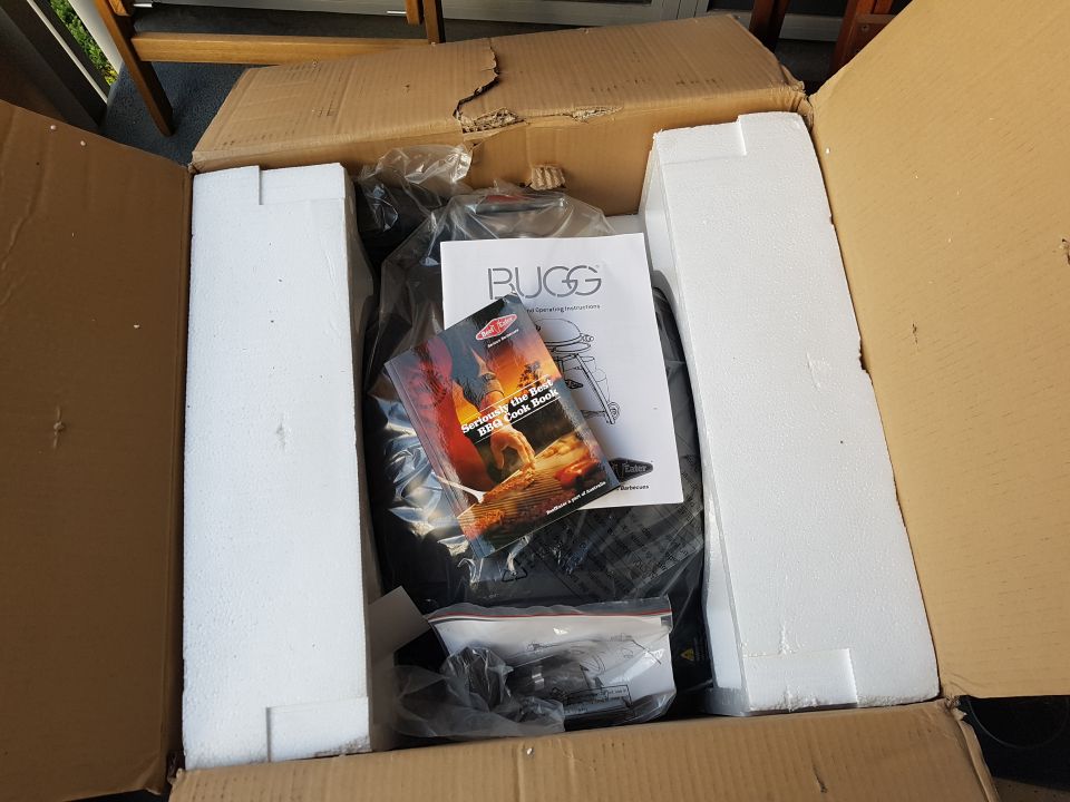 Unpacked barbecue grill with instruction manual and cookbook inside cardboard box