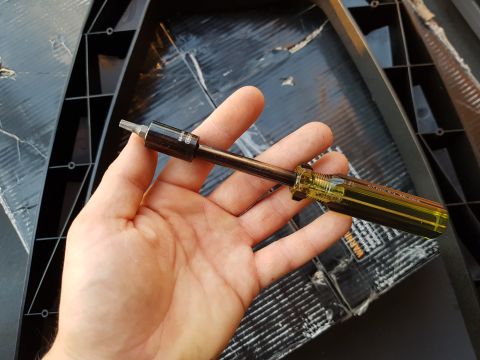 1978 Ford Bronco - A hand holds a screwdriver with a hex bit, positioned over black plastic components.