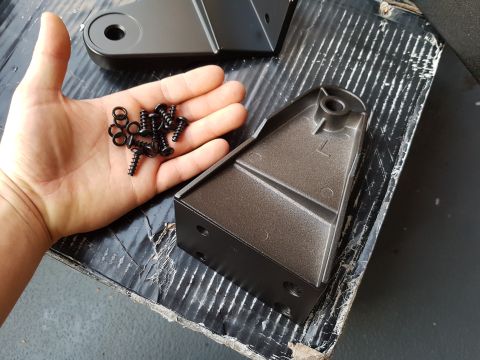 1978 Ford Bronco - A hand holds a collection of black screws and washers near two dark gray metal brackets.