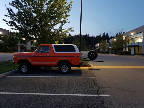 1978 Ford Bronco - Side view of an orange 1978 Ford Bronco with a white hardtop and a rear-mounted spare tire.