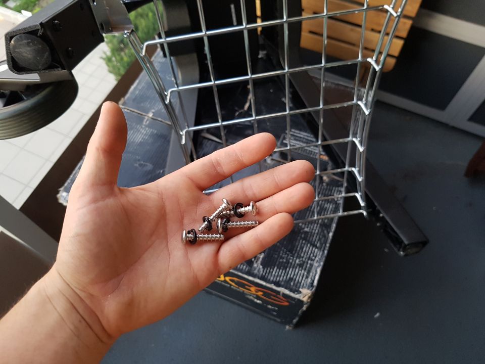 Hand holding several screws with washers near a wire basket structure