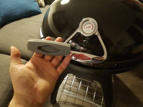 1978 Ford Bronco - A hand holds a gray handle in front of a black BeefEater BBQ grill with a thermometer.