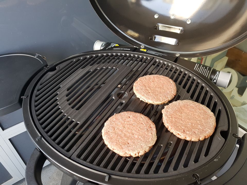 three raw hamburger patties on a black grill with the lid open