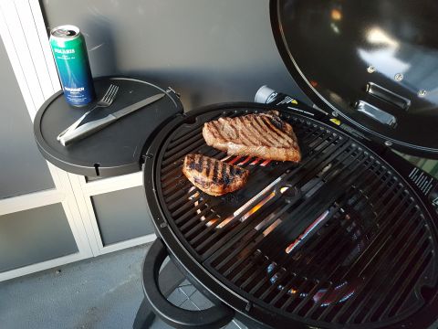 1978 Ford Bronco - Two steaks are grilling on a barbecue with a can of beer and utensils nearby.