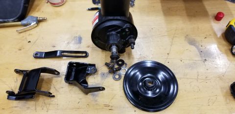 1979 Pontiac Trans Am - Disassembled power steering pump components, including the pump, pulley, and various brackets, are arranged on a workbench.