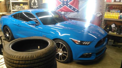 2017 Ford Mustang - A bright blue coupe sits in a garage, with a tire in the foreground and shelves of supplies in the background.