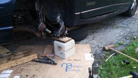 Car's front suspension assembly supported by cinder blocks and wood, with tools nearby