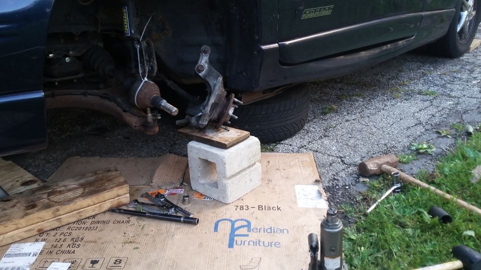 Car's front suspension assembly supported by cinder blocks and wood, with tools nearby