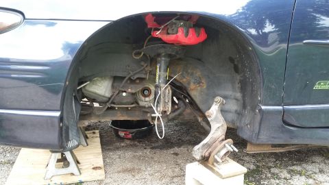 Dark blue car's front wheel assembly removed, with red brake caliper and oil pan visible