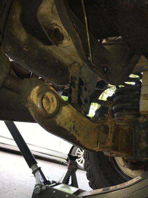 1996 Ford Bronco - The underside of a vehicle is shown, supported by a jack stand, with focus on suspension components.