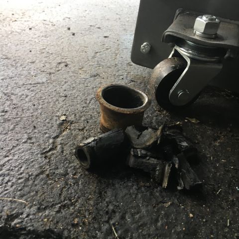 1996 Ford Bronco - Damaged rubber bushings and a metal sleeve lie on the ground near a caster wheel.
