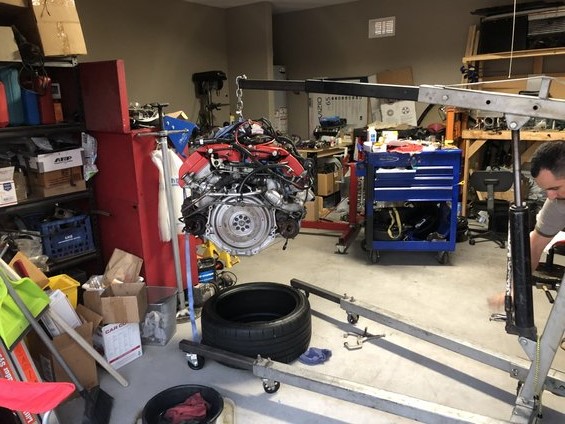 Engine hoisted in garage with tools and parts around