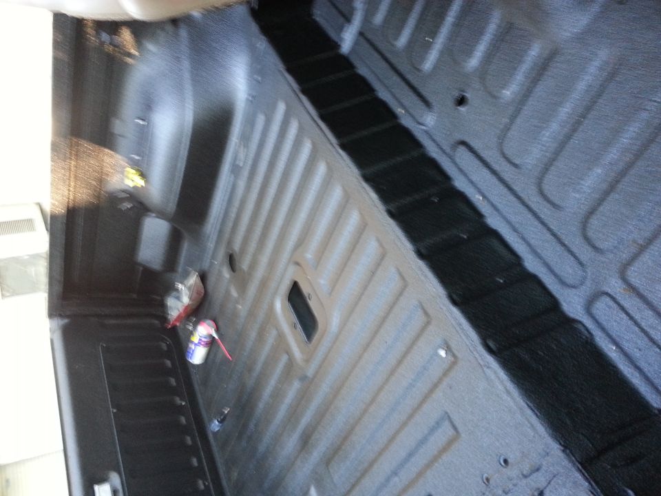 Truck bed interior with spray liner, showing ribbed floor and side panels. A can of spray paint and other items are on the left