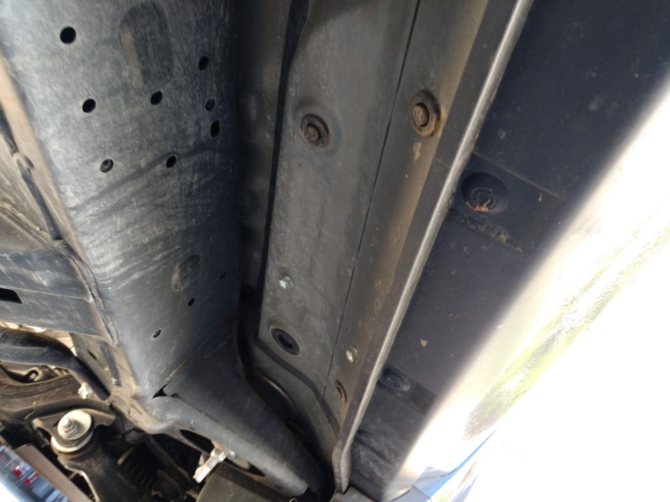 Underside of vehicle frame with bolts and holes, showing running board mounting points