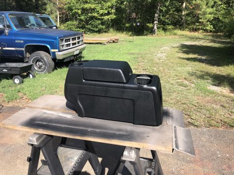 1995 Ford Bronco - A black center console sits on sawhorses outdoors, with a blue pickup truck visible behind it.