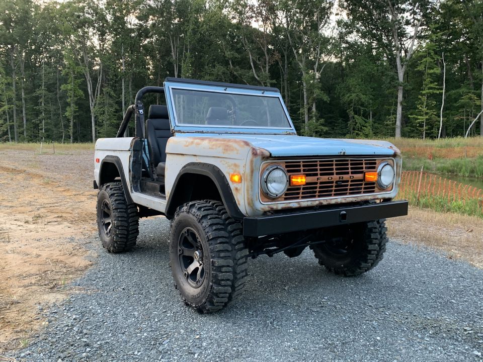 Old Ford Bronco with rust on hood, light blue top, and black bumper