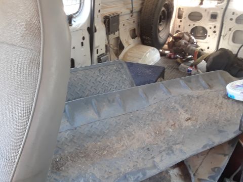 1994 Ford Bronco - The interior of a van is shown, a spare tire mounted on the wall and a transmission on the floor, along with diamond plate flooring.