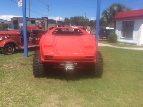 1992 Ford Bronco - A custom red vehicle with oversized tires and a winch is parked on a grassy lot.