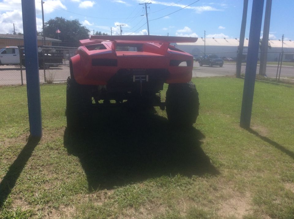 Red custom monster truck with large spoiler and oversized tires, rear view