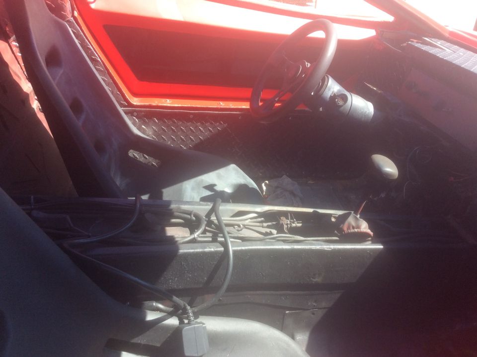 Interior of a red vehicle, showing racing seats, steering wheel, and center console with wiring