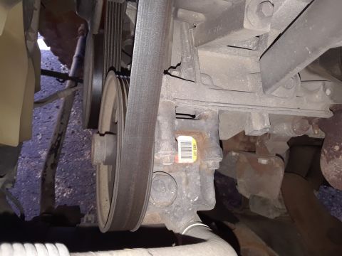 1999 Ford E250 - A close-up view of the engine's belt system and power steering pump, a barcode sticker.