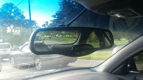 Interior rearview mirror shows traffic on a road, including a dark sedan and a white SUV